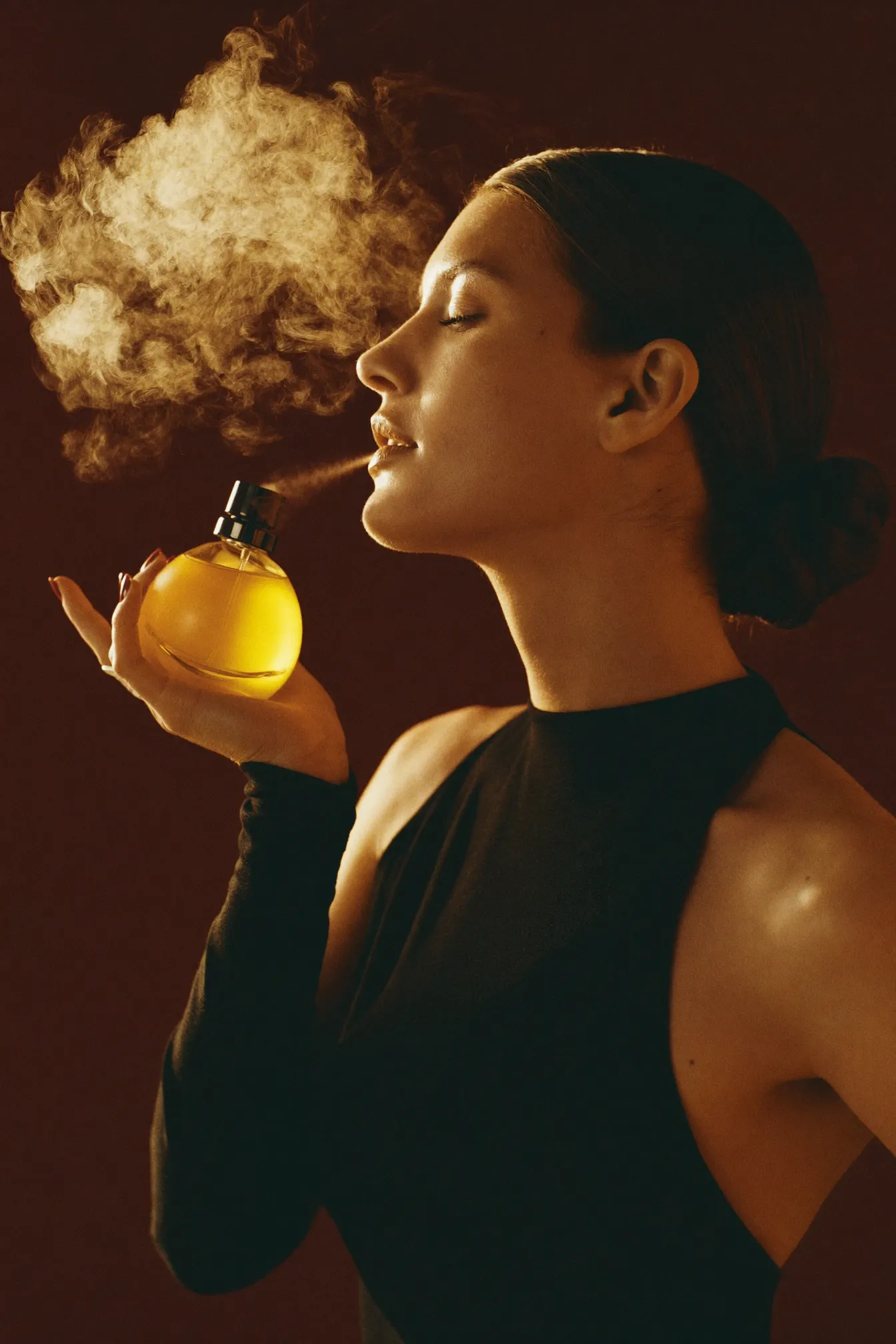 A woman in profile, eyes closed, within a golden mist of fragrance against a bronze backdrop.